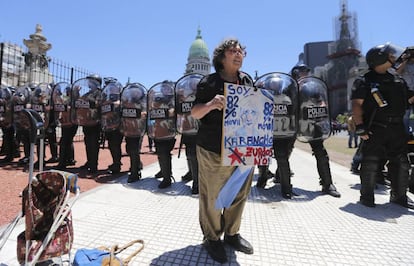 Uma mulher empunha um cartaz contra a reforma da Previdência a alguns passos de distância dos policiais que protegem o legislativo de Buenos Aires.