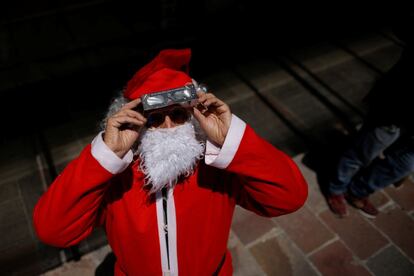 Un hombre disfrazado de Papá Noel usa lentes de protección especiales para observar el eclipse solar.