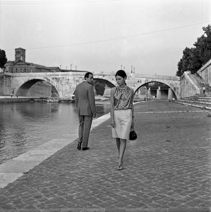 A man and a woman exchange timid glances by a river in Italy circa the 1960s.