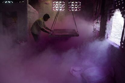 Un trabajador indio sacude polvo de color, conocido como 'gulal', para ser utilizado durante el próximo festival de primavera de Holi, dentro de una fábrica en Fulbari (India).