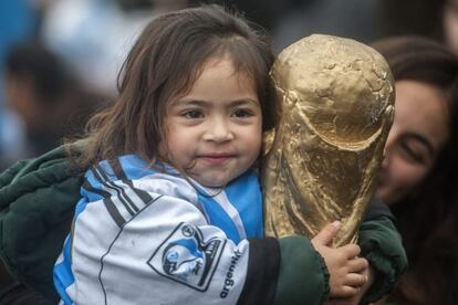 Una ni&ntilde;a sostiene un trofeo de la FIFA al recibir a la selecci&oacute;n Argentina.