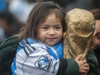 Una ni&ntilde;a sostiene un trofeo de la FIFA al recibir a la selecci&oacute;n Argentina.