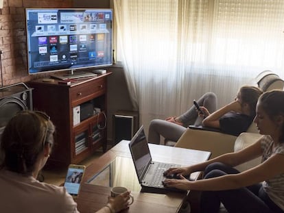 Una joven de Sevilla revisa la oferta de contenidos en Internet a través del televisor mientras su hermana consulta el ordenador y su madre, el móvil.