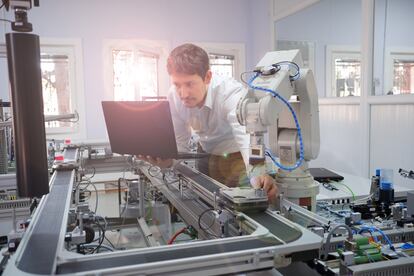 Engineer holding product to teach robot arm position of program and checking on laptop for smart factory automation