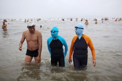 Dos bañistas cubren sus cuerpos con ropa de neopreno y su rostro con un 'facekini' en la playa china de Qingdao.