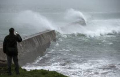 Un hombre fotografía las grandes olas que rompen en un muelle en Esquibien, en la zona oeste de Bretaña, Francia.