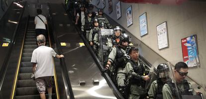 Dos viajeros suben por una escalera mecánica del metro frente a los antidisturbios desplegados para arrestar a los manifestantes en Hong Kong.