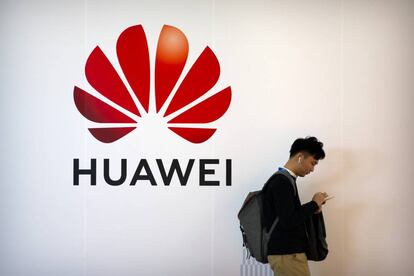 FILE - In this Oct. 31, 2019, filer photo, a man uses his smartphone as he stands near a billboard for Chinese technology firm Huawei at the PT Expo in Beijing.