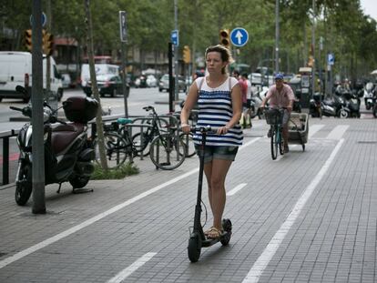 Una mujer circula con un patinete eléctrico por el carril bici de la acera de la Gran Via de Barcelona.