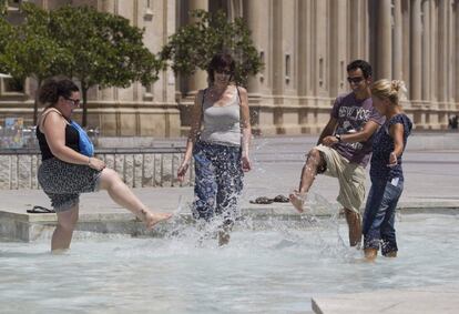 Unos turistas se refrescan en una de las fuentes de la Plaza del Pilar de Zaragoza este mediodía.