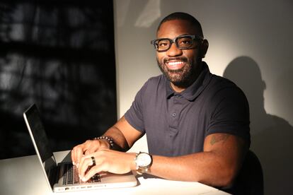 Maynard Okereke - Sitting at a deck with a laptop, smiling,