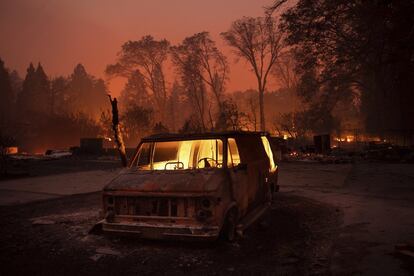 Las llamas iluminan el interior de un vehículo calcinado en un zona de aparcamiento en Paradise, California.