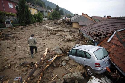 Un hombre pasa junto a un vehículo dañado en una calle cubierta de barro debido a las fuertes inundaciones en la aldea Tekija, Serbia.