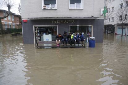 Un grupo de jvenes sentados en un banco observa las inundaciones en el barrio donostiarra de Martutene.