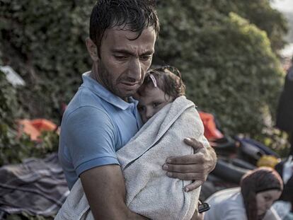 Um homem abraça e seca sua filha ao desembarcarem na ilha de Lesbos, após atravessarem parte do mar Egeu num bote de plástico.