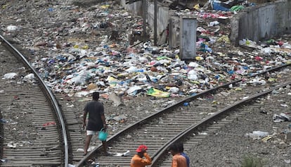 Un hombre camina junto a un montón de basura entre las vías de tren en Bombay.