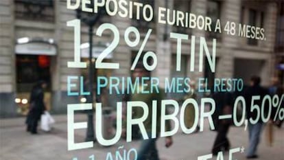 Viandantes reflejados en un escaparate de una entidad bancaria, en Bilbao, con una oferta de depósitos.