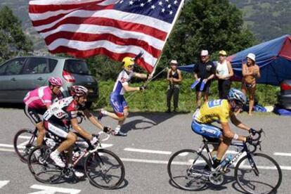 Un aficionado porta una gran bandera de Estados Unidos mientras Armstrong tira de Basso y de Ullrich en la subida de uno de los puertos de la etapa de ayer.