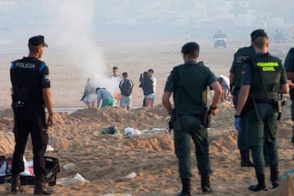 Efectivos de las fuerzas de seguridad esperan a que varios jóvenes abandonen la playa de Nigrán (Vigo), tras la celebración de las hogueras de la noche de San Juan, mientras se llevan a cabo las tareas de limpieza.