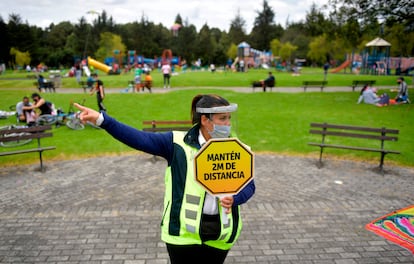 Una vigilante de seguridad con un cartel pidiendo distancia de seguridad, en un parque de Bogotá (Colombia).