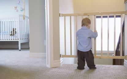 Un bebé sujeta uno de los lados de una barrera de seguridad separadora de estancias.