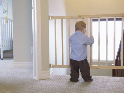 Un bebé sujeta uno de los lados de una barrera de seguridad separadora de estancias.