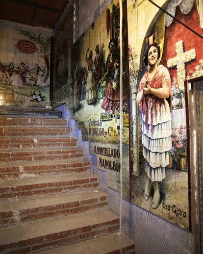 Una escalera que da al primer piso, con un mural de un anuncio de vino amontillados.