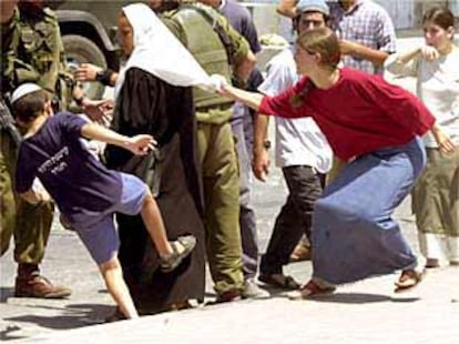 Una joven y un niño israelíes golpean ayer a una mujer palestina en un control militar en la ciudad de Hebrón.