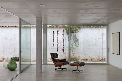 Volcado al porche y al patio con piscina, el salón-comedor es tan esencial como la arquitectura que lo contiene. Junto a la chimenea, la butaca de lectura al lado de las garrafas es un clásico de Charles and Ray Eames, al igual que la silla de madera (ambos los fabrica la empresa alemana Vitra).