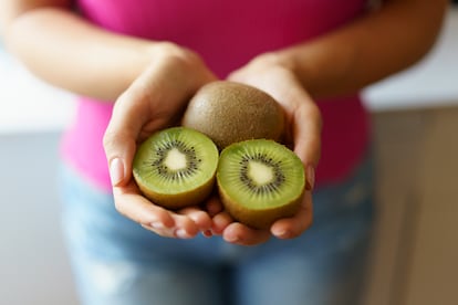 Una mujer sostiene dos kiwis con sus manos.
