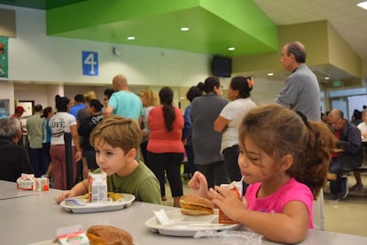 Duas crianças comem enquanto um grupo de pessoas faz fila para obter alimentos em abrigo em Miami, Flórida.
