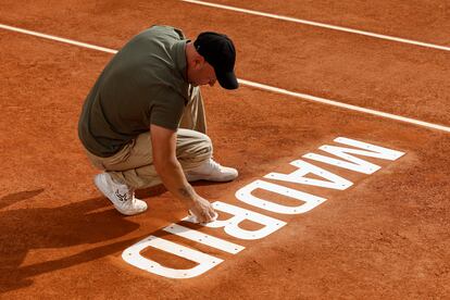 Un técnico de pista repasa el letrero de Madrid de la tierra batida del Mutua Madrid Open.
