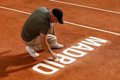 Un técnico de pista repasa el letrero de Madrid de la tierra batida del Mutua Madrid Open.
