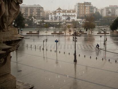 Un solitario ciclista pasea bajo la lluvia frente al palacio de San Telmo en Sevilla.