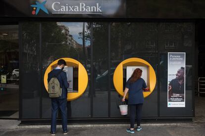 Dvd1020(23/09/20) Una señora limpia un cajero de CaixaBank mientras un chico realiza una operacion en la calle Orense , Pandemia de Coronavirus , Covid19 , Madrid Foto: Víctor Sainz