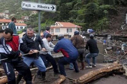 Un grupo de hombres trata de retirar un tronco de un arroyo en Ribeira Brava (Madeira).