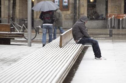 Un hombre aguanta la nieve sentado en un banco del centro de Vitoria, que sufre hoy la cuarta nevada de este año.