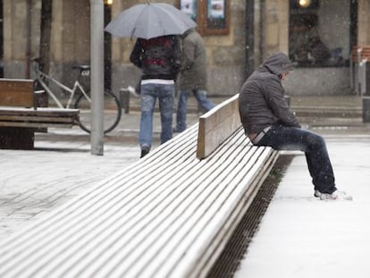 Un hombre aguanta la nieve sentado en un banco del centro de Vitoria, que sufre hoy la cuarta nevada de este año.