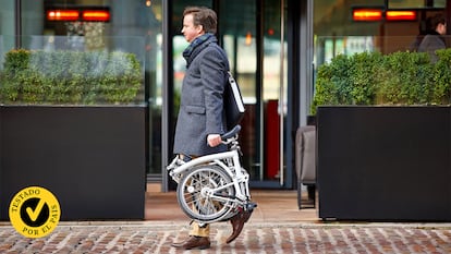 Una hombre caminando por la calle con la bicicleta plegada.