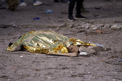 El cuerpo de un civil yace en el suelo cubierto por una manta.