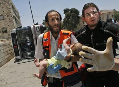 Un médico lleva en brazos a un bebé herido al volcar un autobús que fue embestido por  la excavadora.
