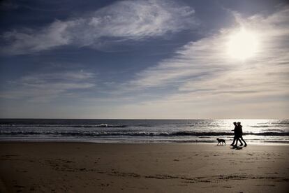 Dos personas junto con su perro pasean por la playa de Mazagón, en Huelva, España. Las buenas temperaturas han hecho que mucha gente en este puente busque la costa.