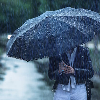 Una persona bajo un lluvia intensa con un paraguas antiviento.