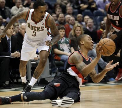 Damian Lillard pasa el balón desde el suelo ante Brandon Jennings