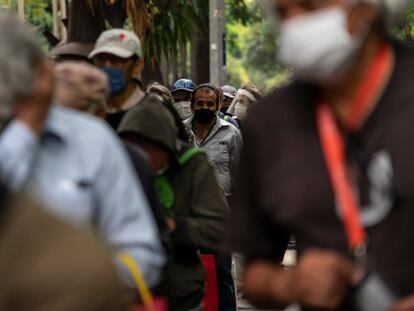 Varios hombres esperan en una fila a recibir alimentos de forma gratuita en la Ciudad de México.
