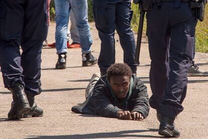 Un inmigrante se encuentra en el suelo rodeado de oficiales de policía franceses en el campo improvisado de Calais (Francia).