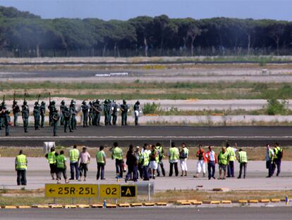 En primer término, los trabajadores de Iberia ocupan, el viernes pasado, las pistas de El Prat. Al fondo, agentes antidisturbios de la Guardia Civil.