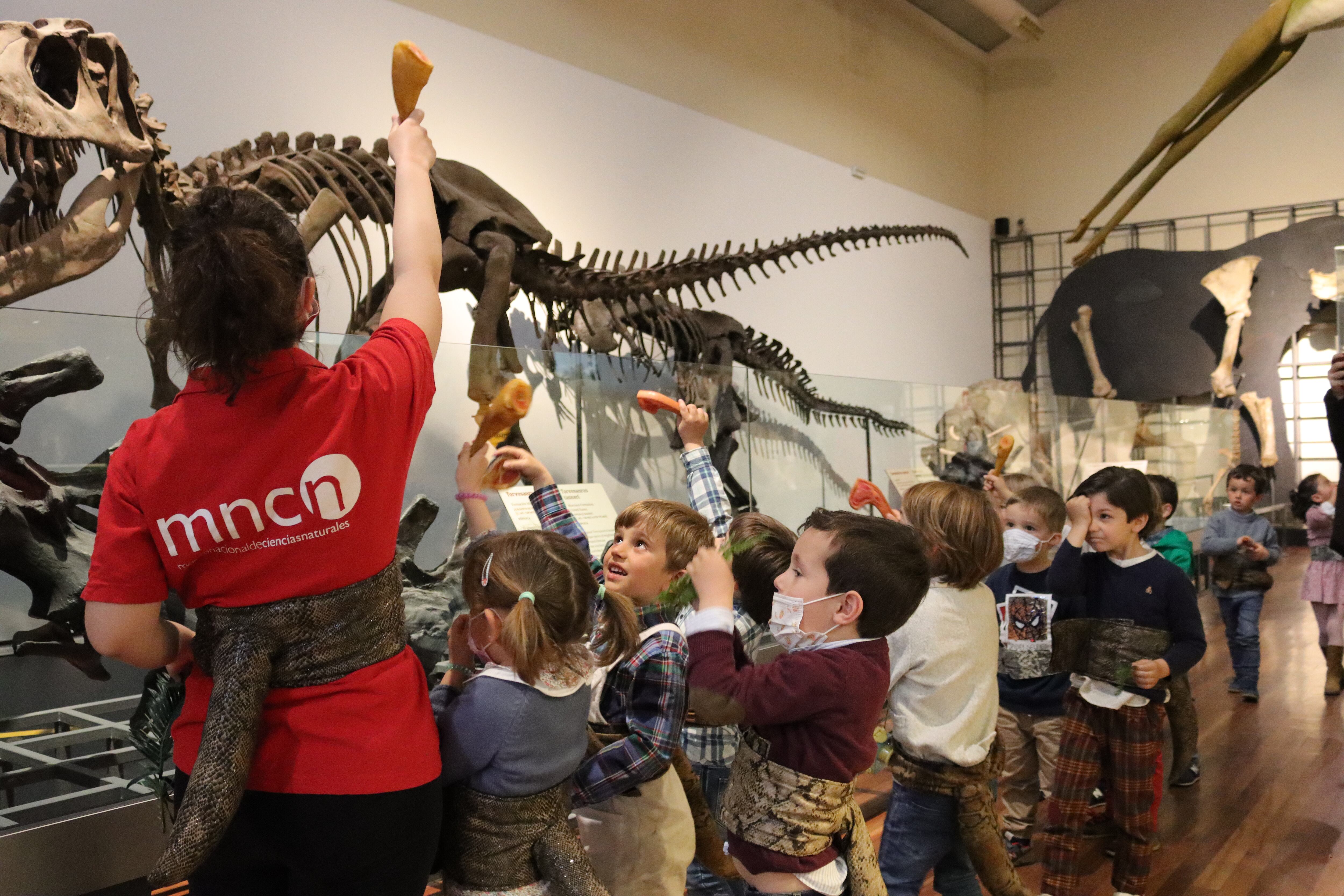 Los niños del taller identifican a un carnívoro durante el recorrido por la exposición de fósiles con sus colas de dinosaurio.