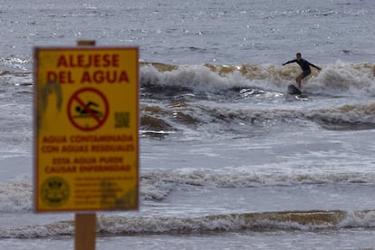 Un surfista ignora un cartel que informa a los bañistas sobre la contaminación del agua en Baja California.
