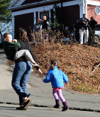 Una madre corre con sus hijos mientras varios policías permanecen a las puertas de una casa en las cercanías del colegio.